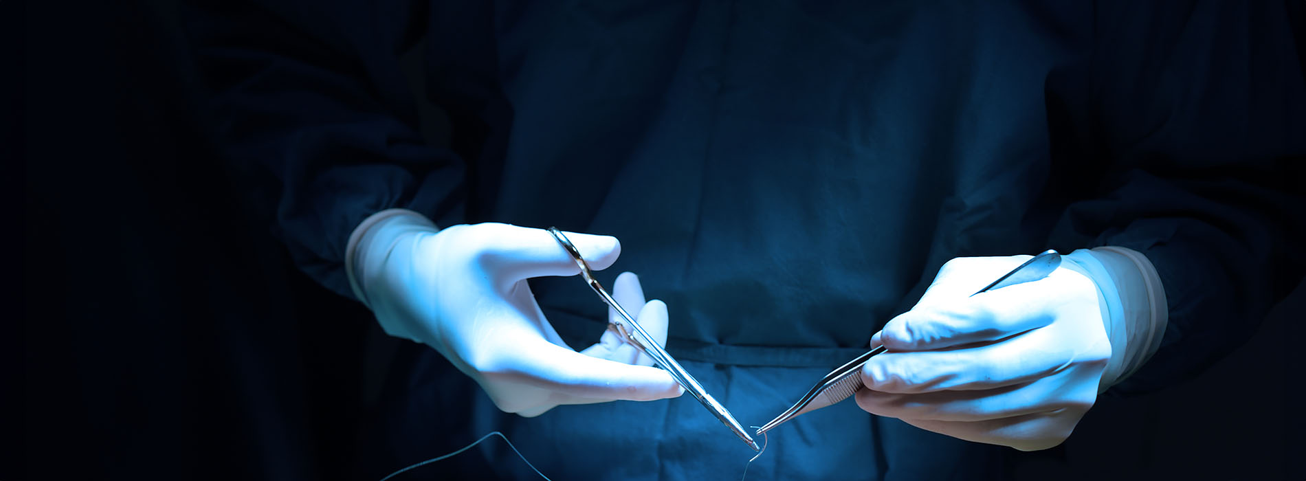 The image shows a pair of hands holding surgical instruments with a blue background.