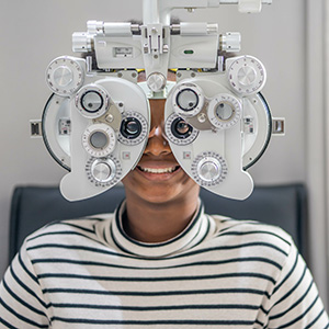 Woman wearing eye glasses with large lenses, sitting in front of an optometrist s machine.