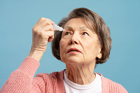 The image shows an elderly woman closely examining a clear object with her hands, possibly for scientific or medical purposes.