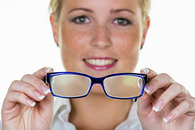 A smiling woman holding blue-framed glasses towards the camera.