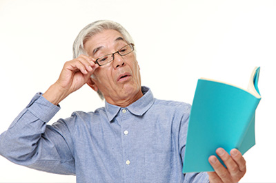 The image shows an elderly man with glasses holding a book, looking surprised or puzzled.