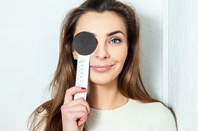 A woman holding a thermometer to her forehead with a measuring tape wrapped around it.